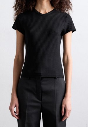 Black ribbed short-sleeve top with a V-neckline, fitted design, and cotton-like texture, paired with high-waisted black trousers.