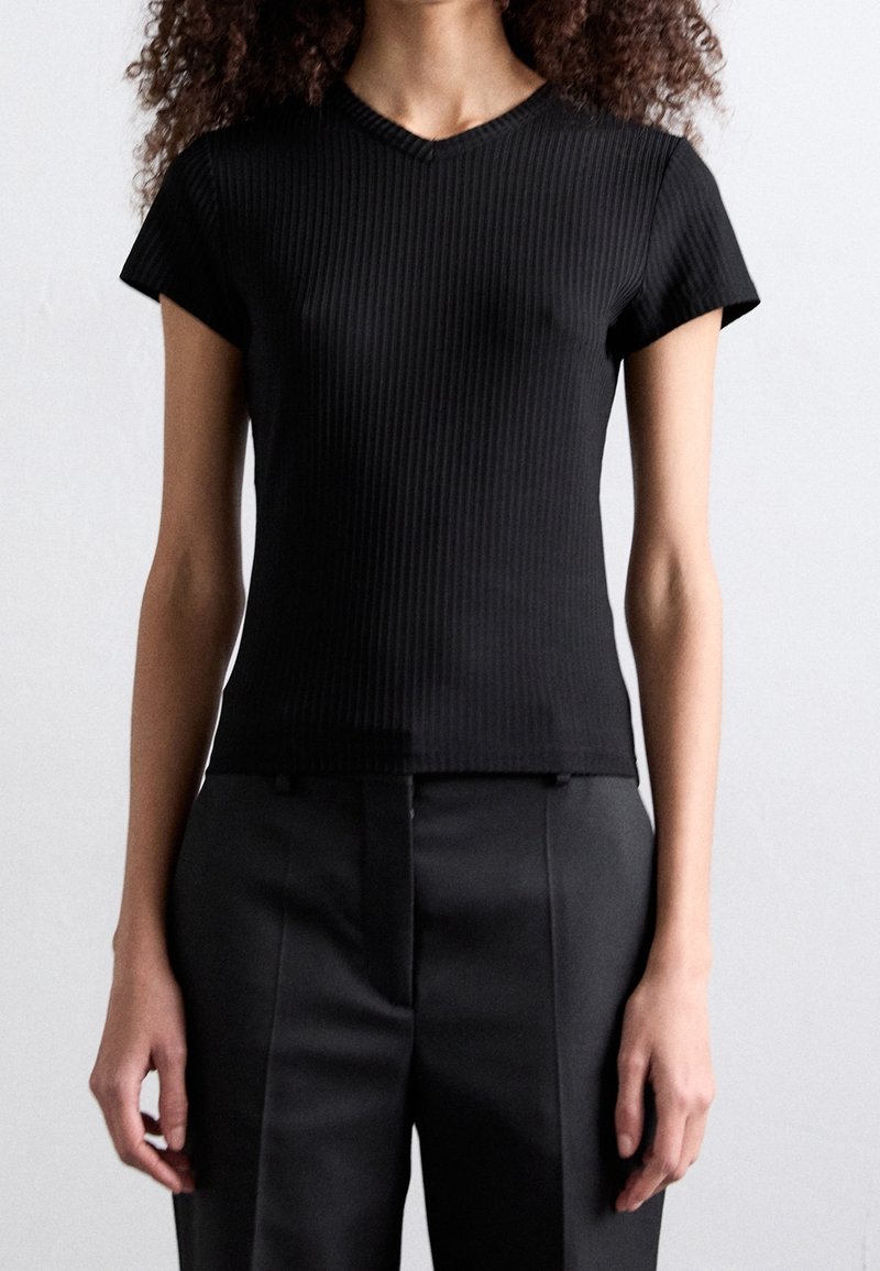 Haut noir côtelé à manches courtes avec un décolleté en V, coupe ajustée et texture semblable au coton, assorti à un pantalon noir taille haute.