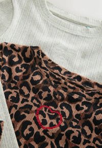 Close-up van twee tops van ribstof, de ene lichtgrijs met een textuurdesign van een strik, de andere in luipaardprint met een rode geborduurde hartdetail.