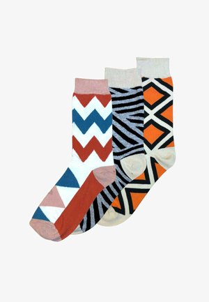 Drie kleurrijke sokken met geometrische patronen: zigzag in wit, blauw, roestkleur en roze; zwarte en grijze zebrastrepen; oranje en zwarte diamantvormen.