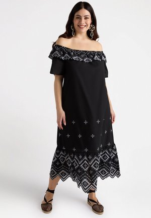 Vestido negro sin mangas con escote caído, detalles fruncidos en el cuello, patrones bordados en blanco y una falda semitransparente con diseños geométricos.