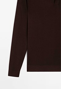 Hnědý dlouhý rukáv top vyrobený z měkké, texturované látky. Má design s výstřihem do V a žebrované manžety. Čistá, minimalistická estetika.