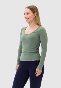 Maglietta a maniche lunghe in verde salvia, con pizzo lungo il collo e bordi ondulati. Tessuto morbido ed elastico con una vestibilità aderente.