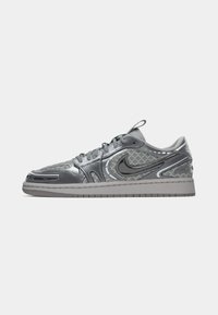 Sneaker grigio con una parte superiore liscia e lucida, dettagli in rete, punta rotonda e suola in gomma grigia. Logo Nike sul lato.