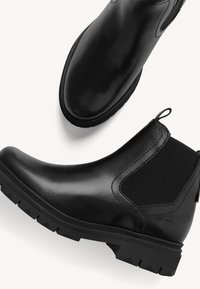 Botine negre din piele cu panouri laterale elastice și talpă din cauciuc texturat. Prezintă un tab de prindere și o finisare netedă.