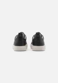 Schwarze Leder-Sneaker mit glatter Oberfläche, weißer Gummisohle und strukturierten Fersenakzenten. Sie verfügen über ein schlankes, flaches Design.