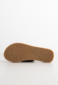 Zwarte schoenzool met een gestructureerd rubberen patroon. Heeft een golvend ontwerp met diamanten vormen. De zool is bruin met een lichte, gripvaste textuur.