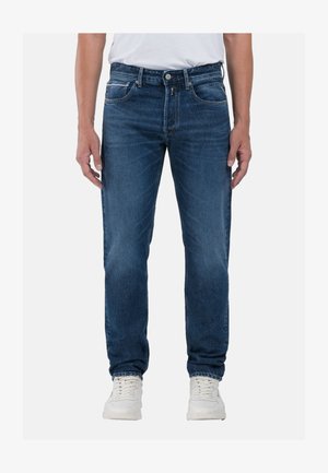 Jeans de mezclilla azul con un corte recto, que cuentan con bolsillos delanteros, cremallera y un ligero desgaste. Combinados con zapatillas blancas.