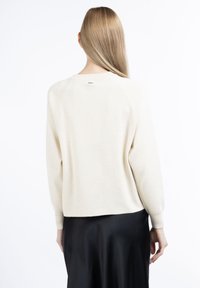 Maglione color crema con maniche a raglan, texture morbida e scollatura tonda, abbinato a una gonna nera fluente.