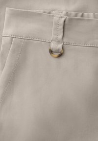 Primer plano de pantalones de tela beige que muestran la pretina cosida, trabilla para cinturón y un pequeño detalle de anilla metálica cerca del bolsillo.