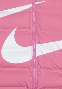 Giacca puffer rosa con finitura lucida. Presenta una cerniera centrale, un grande logo Nike bianco e una texture trapuntata su tutta la superficie.