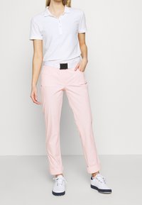 Vit pikétröja med krage, tillsammans med ljusrosa byxor med uppvikt ärm och vita skor med blå accenter. Har ett svart bälte.