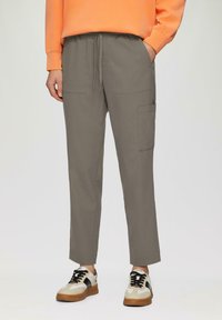 Lichtgrijze joggerbroeken met een elastische tailleband, twee zijzakken en een cargozak op de dij. Gecombineerd met beige en zwarte sneakers.