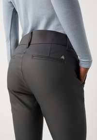Zwarte op maat gemaakte broek met een gladde textuur, een achterzak met een rits en subtiele merknamen bij de zak.