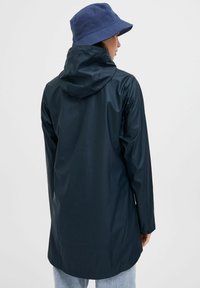 Navy waterproof jacket with a hood, long sleeves, and a relaxed fit. Paired with a blue bucket hat. Smooth texture with no prominent patterns.