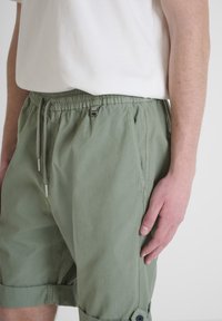 Pantaloni shorts verde chiaro realizzati in un tessuto morbido e testurizzato. Vita elasticizzata con cordoncino, tasche laterali e risvolti fissati da bottoni.