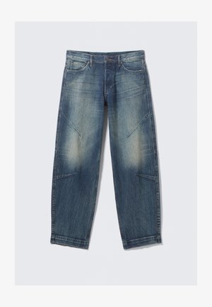 Jeans de denim azul desgastado con bolsillos frontales, un cierre de botón y cremallera, y detalle de costura en ángulo en las piernas.
