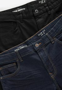 Dos pares de jeans ajustados: uno negro con textura suave y otro azul oscuro con detalles de costura visibles, con cinturillas de marca.