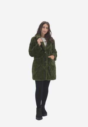 Green faux fur coat with a notched collar, two front pockets, and button closure, worn over black leggings and boots. Smooth, plush texture.