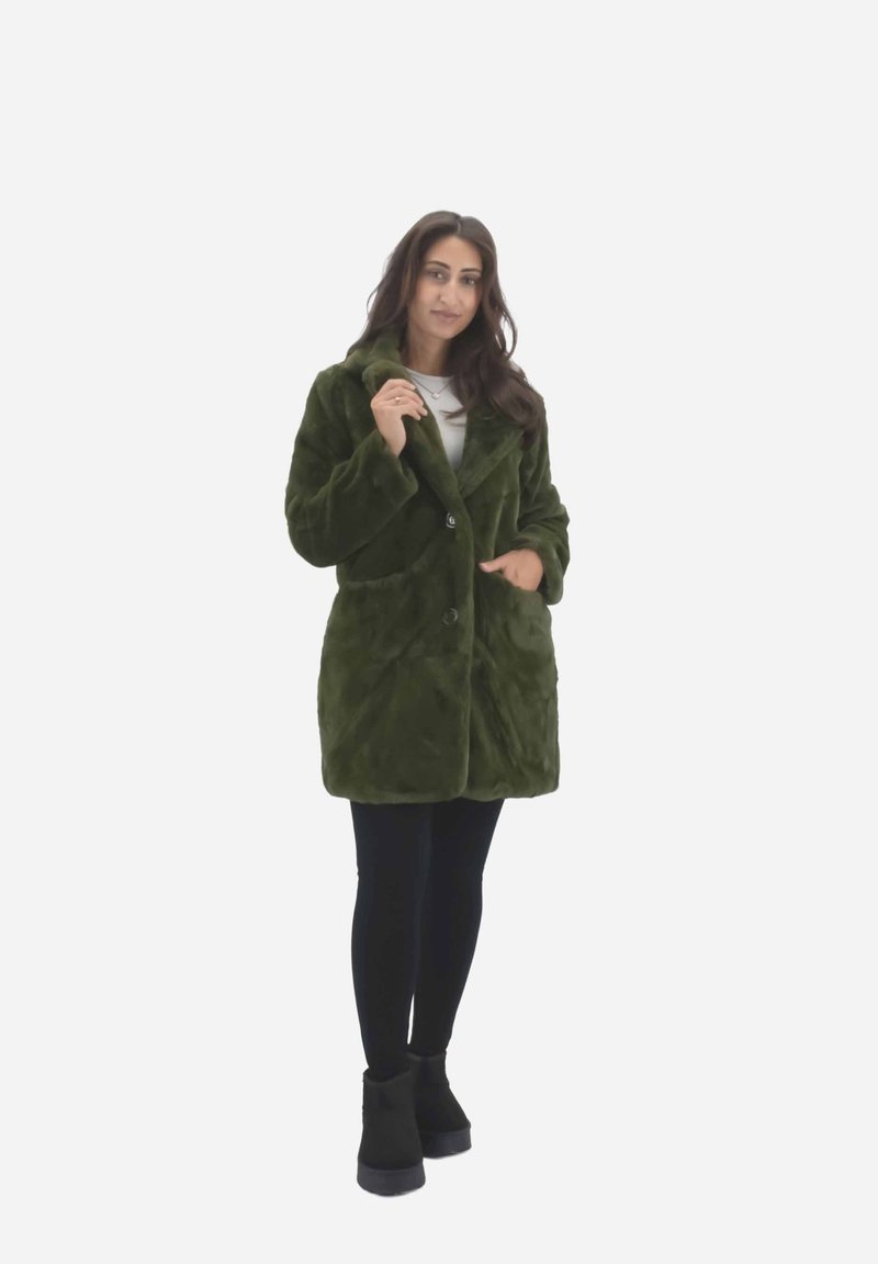 Cappotto di pelliccia sintetica verde con colletto a punte, due tasche frontali e chiusura con bottoni, indossato su leggings neri e stivali. Tavolozza liscia e vellutata.