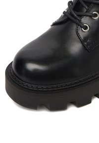 Czarne skórzane botki za kostkę z okrągłym noskiem, grubą teksturowaną podeszwą i metalowymi oczkami na sznurowadła. Gładkie wykończenie z widocznym szwem.
