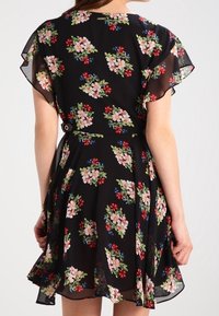 Robe noire à motifs floraux avec des manches courtes évasées, ornée d'impressions de fleurs colorées en rose, rouge et bleu, et une taille cintrée avec un détail de ceinture.