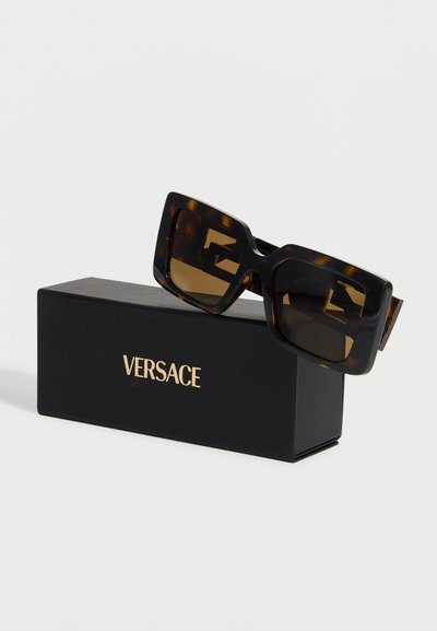 Ορθογώνια γυαλιά ηλίου με σχέδιο χελώνας και σκούρους φακούς ακουμπισμένα σε μαύρο κουτί με το λογότυπο της Versace.