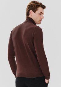 Brązowy sweter typu golf wykona ny z miękkiego materiału dzianinowego, z dopasowanym krojem, prążkowanymi mankietami i detalami na dolnej krawędzi, pokazany od tyłu.