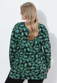 Tunica a maniche lunghe in tessuto nero con motivi paisley verdi e blu. Il design sul retro presenta un orlo curvo e spacco laterale.