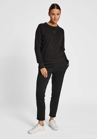 Svart sweatshirt och byxor i ett mjukt tyg med avslappnad passform. Anmärkningsvärt logodetalj på bröstet, tillsammans med vita sneakers.