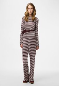 Gestreepte jumpsuit met lange mouwen in kastanjebruin en crème, voorzien van een getailleerde taille met bijpassende riem. Zachte, geribbelde textuur met wijde pijpen.