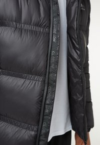 Giubbotto puffo nero realizzato in materiale leggero, con design trapuntato e zip prominente con il marchio "CLOSURE LDN" lungo l'apertura.