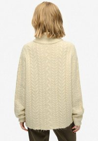 Cream-colored oversized sweater featuring a high neck, cable knit design, loose fit, and ribbed cuffs, with a soft, textured finish.