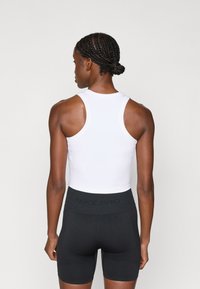 Biała dopasowana koszulka na ramiączkach zestawiona z czarnymi szortami Nike Pro. Koszulka ma okrągły dekolt i bezrękawowy fason, natomiast szorty mają wysoki stan.