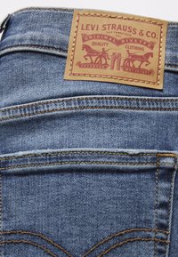Blaue Jeans aus Denim mit einem braunen Lederpatch, das rote Druckdetails enthält, darunter "LEVI STRAUSS & CO." und zwei silhouettierte Pferde.
