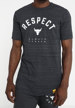 Ciemnoszara koszulka z krótkim rękawem z napisem „RESPECT” i logo byka nad napisem „ALWAYS EARNED”, noszona z dopasowanymi ciemnoszarymi szortami z logo i napisem.