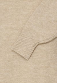 Manche de pull en tricot beige avec bord-côtes sur un fond en tissu tricoté beige assorti.