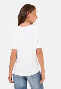 T-shirt bianco in cotone con maniche corte, scollatura rotonda e vestibilità rilassata. Tessuto liscio con una leggera lucentezza e dettagli di cucitura visibili.