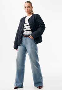 Granatowa pikowana kurtka z zatrzaskami, zestawiona z biało-granatowym paskowanym topem i jasnoniebieskimi szerokimi dżinsami. Brązowy pasek i bordowe buty.