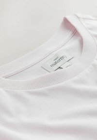 Šviesiai rožinė nėščiųjų marškinėliai su apvalia iškirpte, ribbingo audinio apdaila ir etikete, kurioje parašyta „NEXT maternity“. Lygios medvilnės audinio tekstūra.