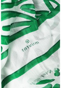 Sciarpa verde e bianca con motivi astratti a foglia, realizzata in tessuto leggero con bordi frangiati, marchiata con il logo circolare "TNTUUM".