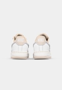 Valkoiset nahkakengät, joissa on beige ja harmaa korostus. Varusteena pehmustettu nilkkareuna, teksturoitu pohja ja "NIKE"-brändäys kantapäässä.