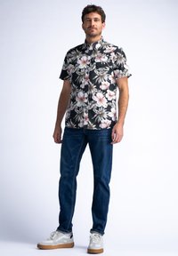 Camisa de flores negra de manga corta con flores rosas y blancas, combinada con jeans azules y zapatillas deportivas claras con acentos grises y beige.