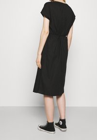 Robe noire à manches courtes, taille cintrée et ourlet au genou. Portée avec des baskets montantes noires. Tissu simple et texturé.