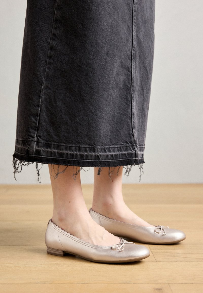 Weiche, metallische Blush-Balletschuhe mit gewelltem Rand und Schleifendetail, kombiniert mit einem fransigen, dunklen Jeansrock. Flacher Absatz und glatte Textur.