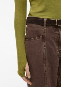 Halenka s dlouhým rukávem olivově zelené barvy spárovaná s džínovými kalhotami tmavě hnědé barvy s vysokým pasem, které mají jemnou texturu a kontrastní švy.