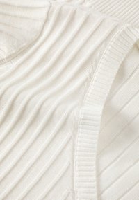 Tejido blanco de punto acanalado con rayas texturizadas de diferente grosor, que presenta un acabado suave y variaciones sutiles en el grosor a lo largo de los bordes.