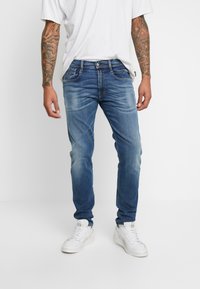 Jeans din denim albastru, cu o croială normală, ușor decolorate, design cu cinci buzunare și închidere cu buton, asortate cu adidași albi și un tricou gri.