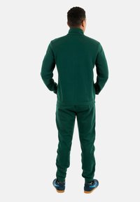 Chándal verde hecho de una tela suave, con cuello alto y puños elásticos, combinado con zapatillas que tienen acentos en azul.