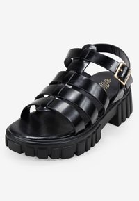 Sandalo platform nera con ampie cinghie orizzontali, cinturino alla caviglia con fibbia e suola spessa e texturizzata. Realizzato in materiale sintetico liscio.